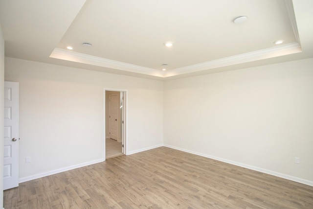 spare room featuring ornamental molding, a raised ceiling, and light wood-type flooring