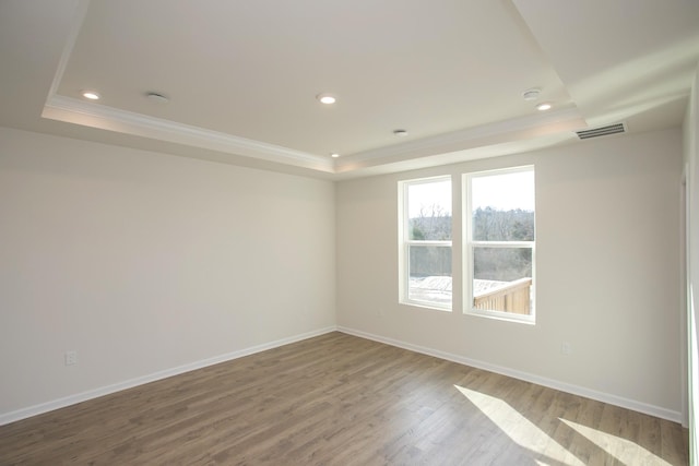 spare room with a raised ceiling, wood-type flooring, and ornamental molding