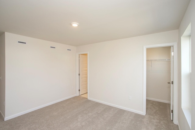 unfurnished bedroom with a closet, a spacious closet, and light carpet