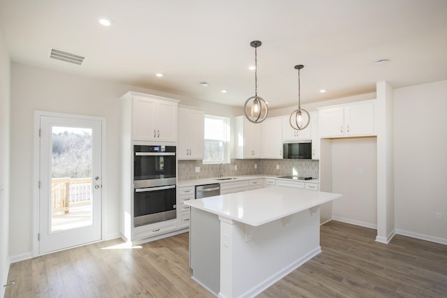 kitchen featuring white cabinetry, tasteful backsplash, a center island, light wood-type flooring, and stainless steel appliances