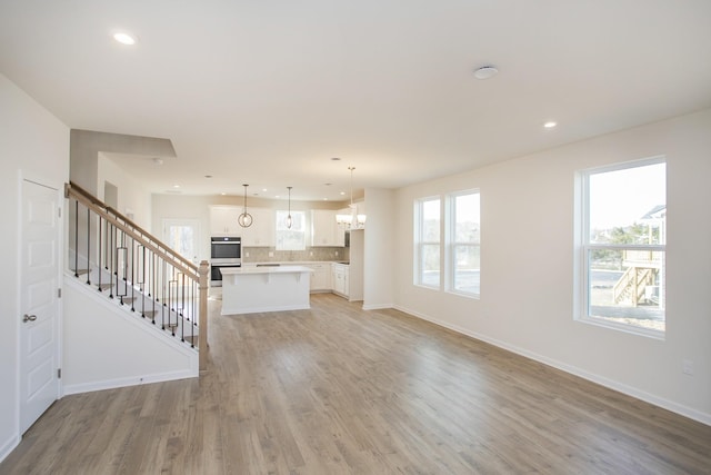 unfurnished living room featuring an inviting chandelier and light hardwood / wood-style floors