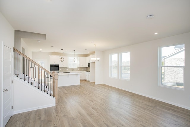 unfurnished living room featuring an inviting chandelier and light hardwood / wood-style flooring