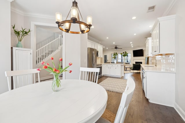 dining room featuring ornamental molding, ceiling fan with notable chandelier, dark wood-type flooring, and sink