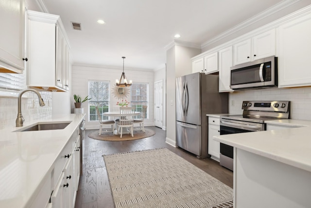 kitchen featuring appliances with stainless steel finishes, pendant lighting, white cabinetry, sink, and ornamental molding