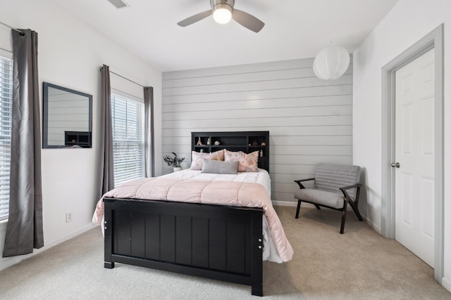 bedroom with light carpet, wooden walls, and ceiling fan