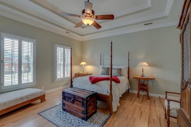 bedroom with a raised ceiling, crown molding, and light wood-type flooring