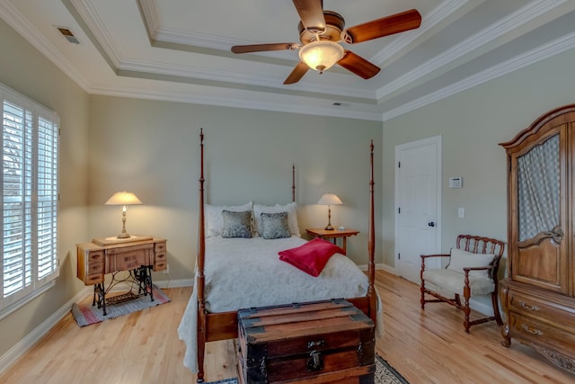 bedroom with multiple windows, a tray ceiling, and wood-type flooring