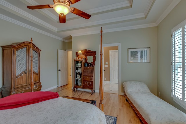 bedroom featuring multiple windows, a tray ceiling, crown molding, and light wood-type flooring