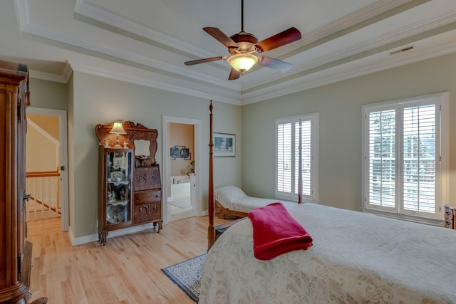 bedroom with crown molding, ensuite bathroom, a tray ceiling, and light hardwood / wood-style floors