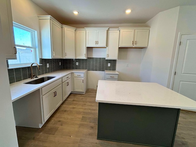 kitchen featuring sink, a center island, white cabinets, hardwood / wood-style floors, and backsplash