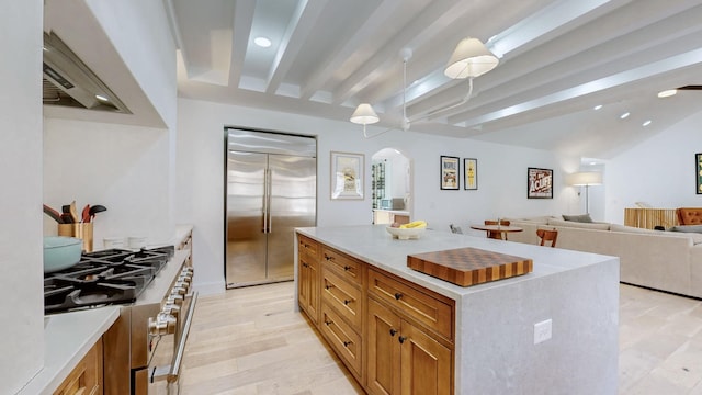 kitchen with lofted ceiling with beams, appliances with stainless steel finishes, a center island, and light hardwood / wood-style flooring