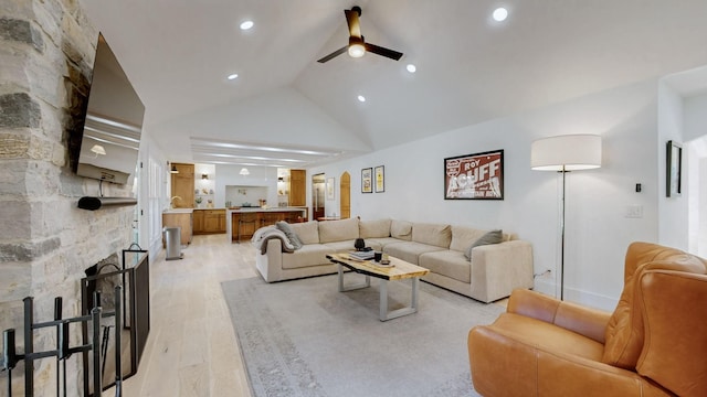 living room featuring ceiling fan, a stone fireplace, high vaulted ceiling, and light hardwood / wood-style floors