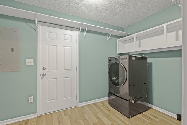 clothes washing area featuring washer / dryer, light hardwood / wood-style flooring, electric panel, and a textured ceiling