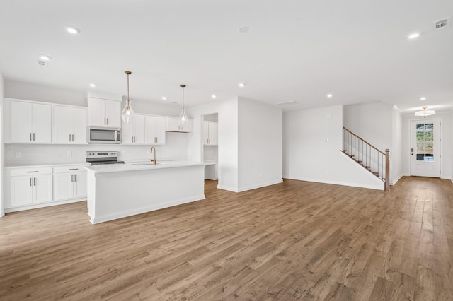 kitchen featuring white cabinetry, an island with sink, sink, light hardwood / wood-style floors, and stainless steel appliances