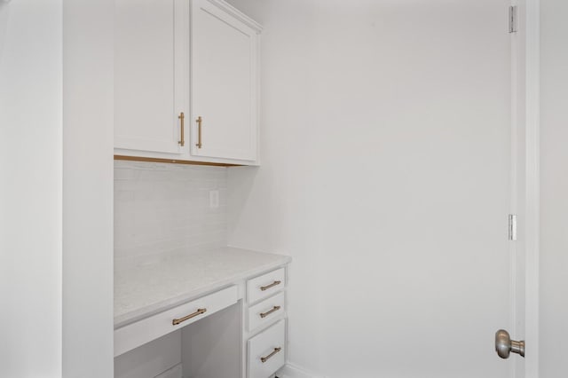 interior space featuring backsplash, light stone counters, and white cabinets