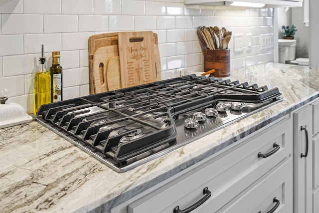 details with light stone counters, backsplash, and stainless steel gas cooktop