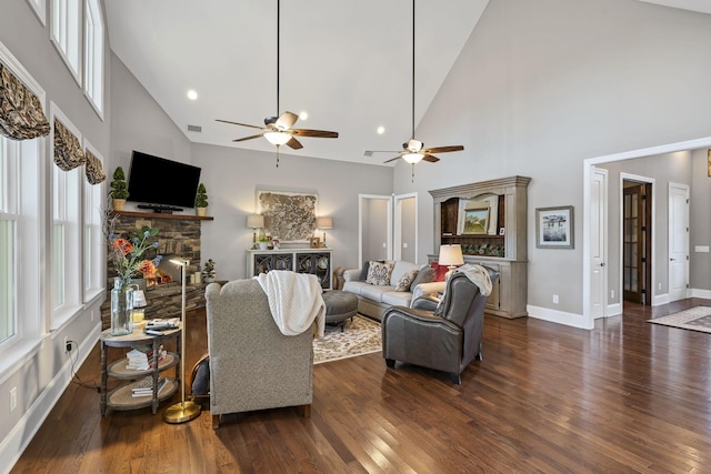 living room featuring a stone fireplace, dark hardwood / wood-style floors, ceiling fan, and a high ceiling