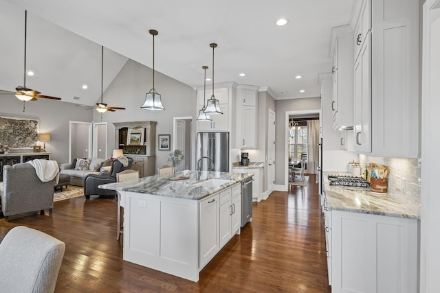 kitchen with white cabinetry, appliances with stainless steel finishes, light stone countertops, and a center island with sink