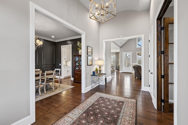 foyer with ornamental molding, lofted ceiling, dark wood-type flooring, and an inviting chandelier