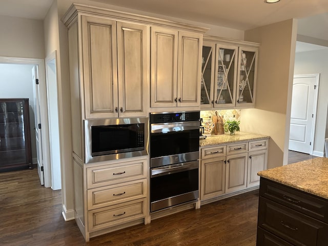 kitchen featuring light stone counters, cream cabinets, dark hardwood / wood-style flooring, and appliances with stainless steel finishes