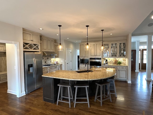 kitchen with a kitchen bar, sink, ornate columns, appliances with stainless steel finishes, and a kitchen island with sink