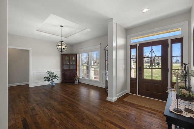 foyer entrance with dark wood-type flooring, a tray ceiling, and wainscoting