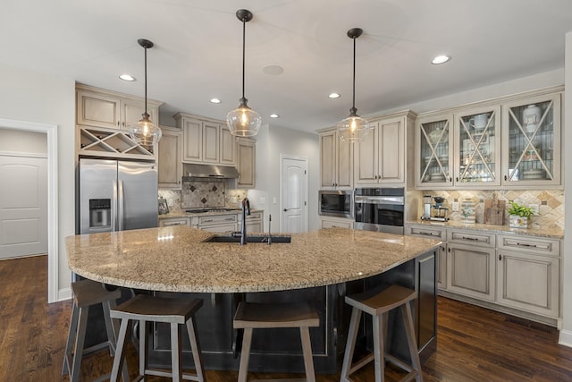 kitchen with a center island with sink, a breakfast bar, cream cabinets, stainless steel appliances, and a sink