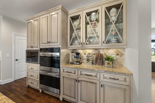 kitchen featuring light stone counters, dark wood finished floors, backsplash, cream cabinets, and stainless steel double oven