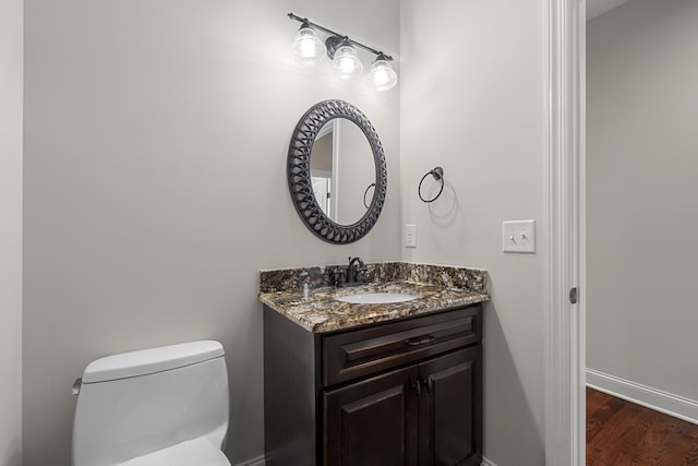 bathroom featuring toilet, baseboards, wood finished floors, and vanity