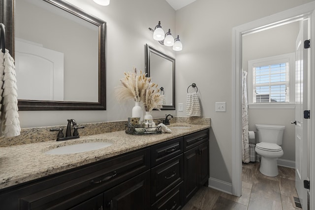 bathroom with double vanity, a sink, toilet, and baseboards