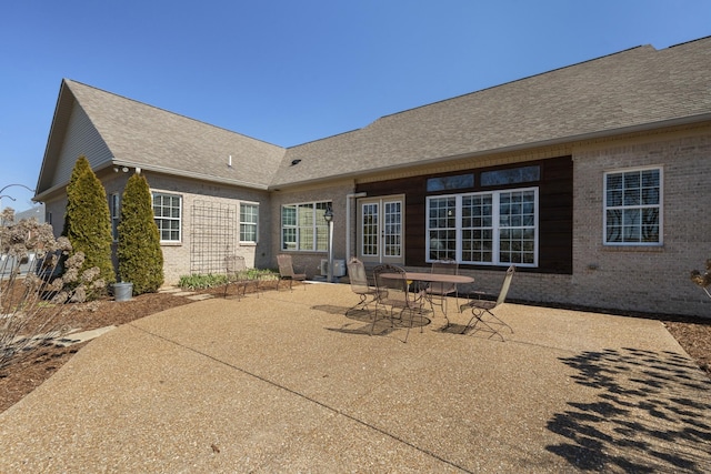 rear view of house with a shingled roof, brick siding, and a patio