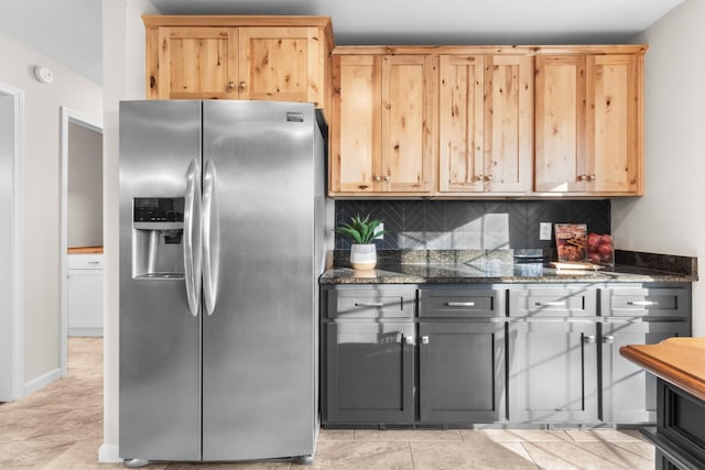 kitchen featuring light brown cabinets, stainless steel fridge, backsplash, and dark stone counters