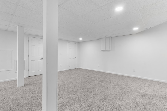 basement with a paneled ceiling and light colored carpet