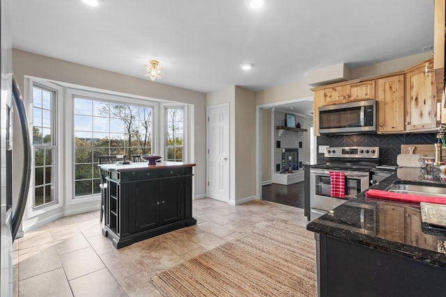 kitchen with dark stone countertops, backsplash, stainless steel appliances, a center island, and light brown cabinetry