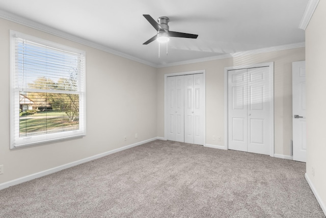 unfurnished bedroom with crown molding, two closets, ceiling fan, and carpet flooring