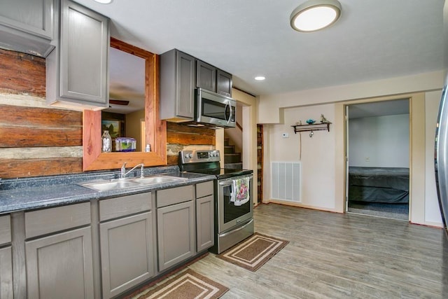 kitchen with gray cabinetry, sink, light hardwood / wood-style flooring, and appliances with stainless steel finishes