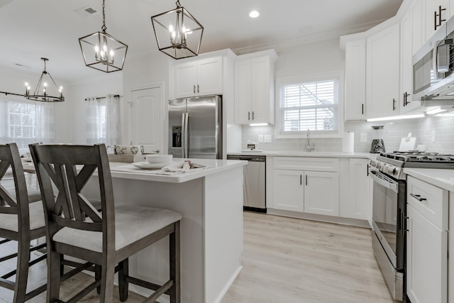 kitchen with crown molding, stainless steel appliances, a kitchen breakfast bar, white cabinets, and decorative light fixtures