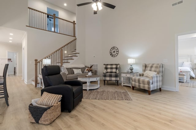 living room with ceiling fan, a towering ceiling, and light hardwood / wood-style floors