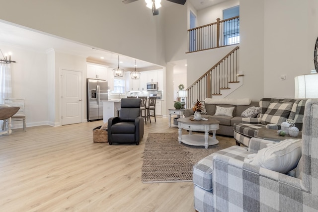 living room featuring ceiling fan with notable chandelier, light hardwood / wood-style floors, and a high ceiling