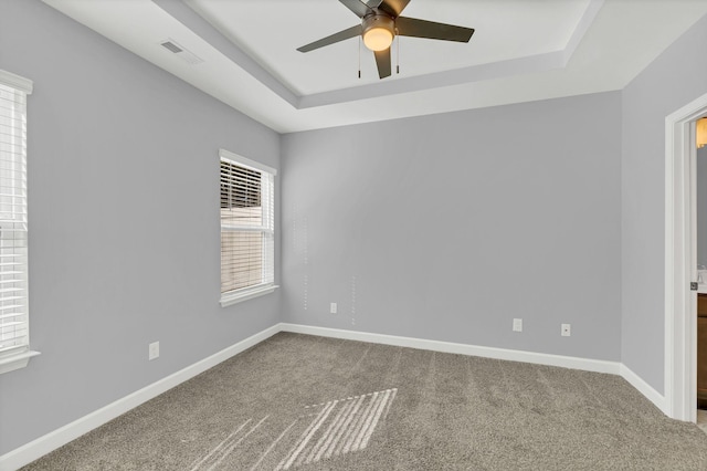 empty room with ceiling fan, carpet flooring, and a tray ceiling