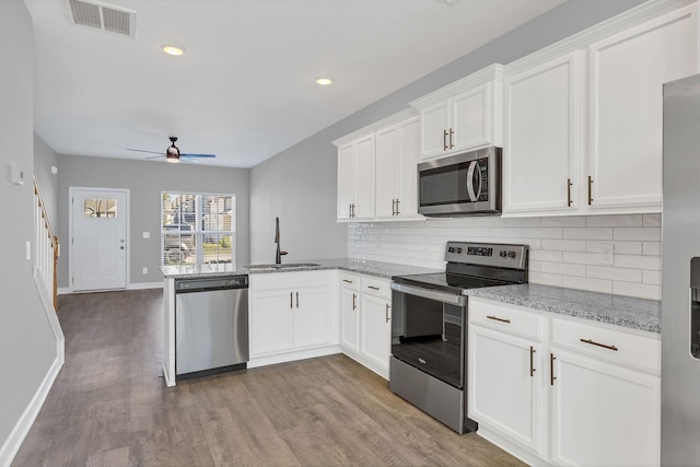 kitchen with sink, white cabinets, kitchen peninsula, stainless steel appliances, and light stone countertops