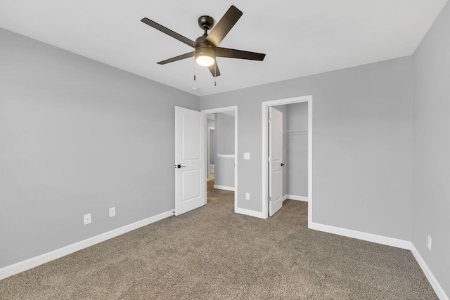 unfurnished bedroom with a walk in closet, a closet, ceiling fan, and carpet flooring