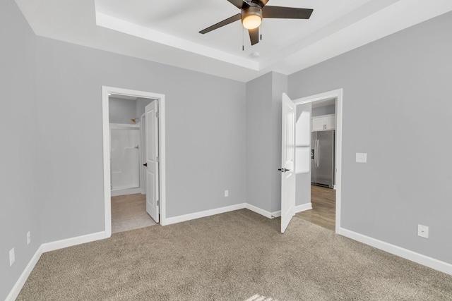 unfurnished bedroom featuring a raised ceiling, stainless steel refrigerator with ice dispenser, connected bathroom, and light carpet