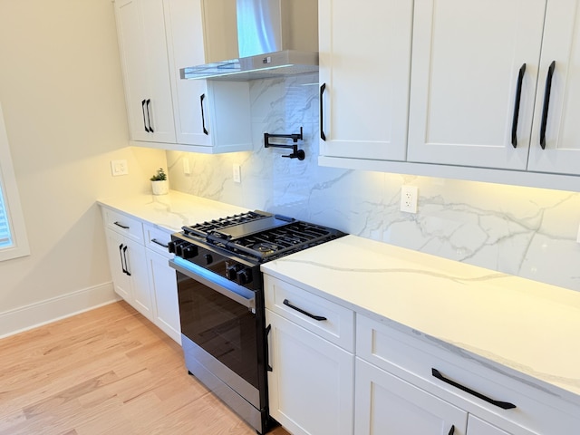 kitchen featuring wall chimney exhaust hood, gas range oven, light stone countertops, and white cabinets