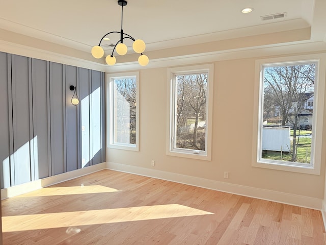 empty room with an inviting chandelier, a tray ceiling, a wealth of natural light, and light wood-type flooring