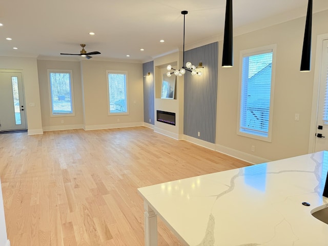 kitchen with light stone counters, decorative light fixtures, light hardwood / wood-style floors, and crown molding