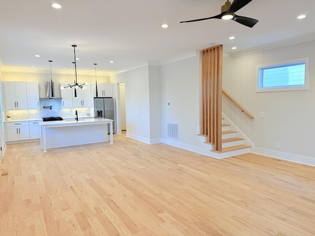 kitchen with white cabinetry, stainless steel fridge with ice dispenser, a center island with sink, ornamental molding, and pendant lighting