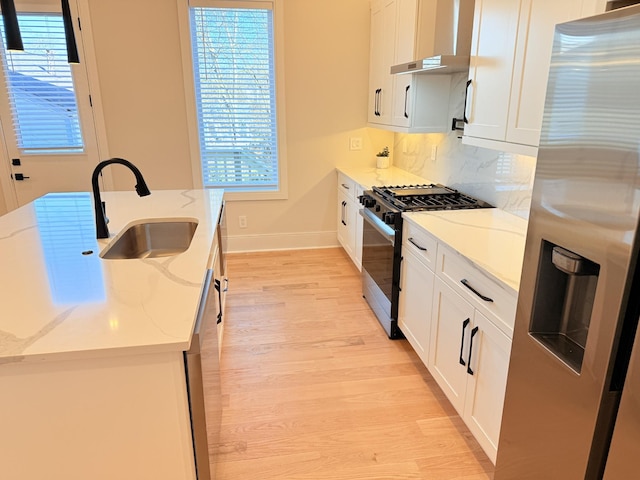 kitchen featuring appliances with stainless steel finishes, sink, white cabinets, light stone countertops, and light hardwood / wood-style flooring