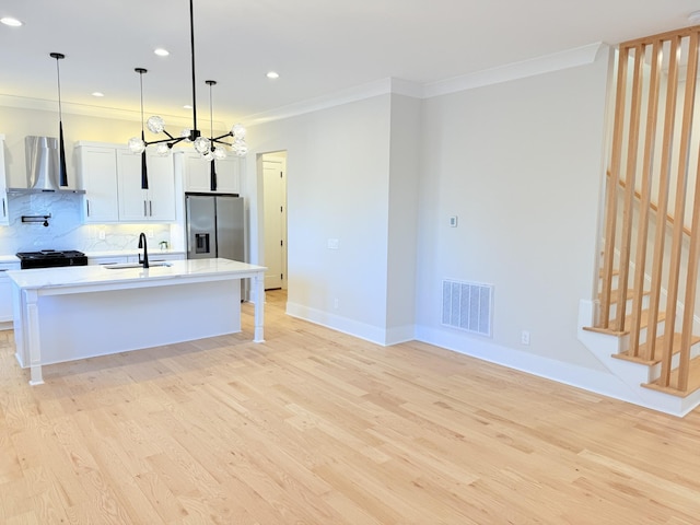 kitchen featuring white cabinetry, hanging light fixtures, stainless steel fridge, and wall chimney exhaust hood