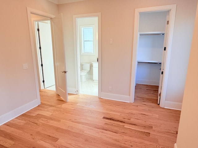 unfurnished bedroom with a spacious closet, connected bathroom, light hardwood / wood-style floors, and a closet